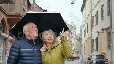 中年妇女和她<strong>年迈</strong>的丈夫一起在户外站在铺好的街道上，撑着伞